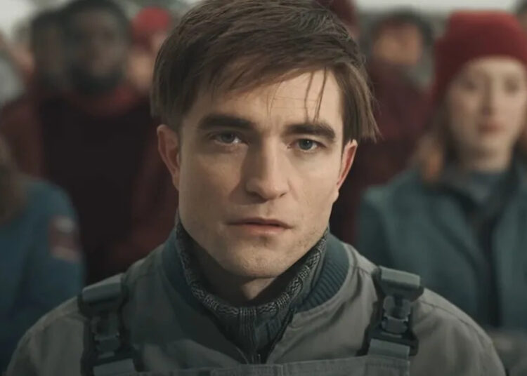 Robert Pattinson sits with a neutral expression in the sunlight in Mickey 17.