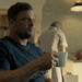 Alan Ritchson's Jack Reacher holds a coffee mug as he sits at a kitchen table in Reacher
