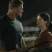 Alan Ritchson as Jack Reacher standing next to Sonya Cassidy as Susan Duffy in front of a table full of guns in Reacher