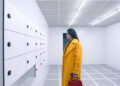 Elisabeth in her yellow coat staring at lockers in The Substance