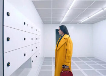 Elisabeth in her yellow coat staring at lockers in The Substance