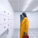 Elisabeth in her yellow coat staring at lockers in The Substance