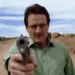 Bryan Cranston's Walter White points a pistol at the camera while standing in a desert in Breaking Bad