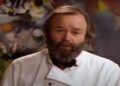 A middle aged caucasian man with brown hair wearing a white chef's jacket with his eyebrows scrunched