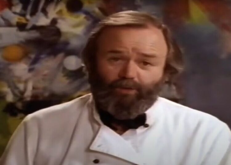 A middle aged caucasian man with brown hair wearing a white chef's jacket with his eyebrows scrunched