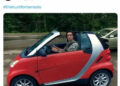 Adam Driver in a red Smart Car staring at the camera seriously.