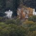 A drone shot of a white mansion pictured through a dense forest.