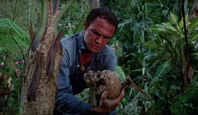 Burt Reynolds as Douglas Temple holding a skull in Skullduggery
