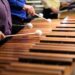 Musicians in purple and blue shirts hold mallets and play a marimba. Furman Percussion Ensemble