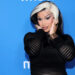 Cardi B with black and white hair poses against a blue background wearing a black outfit.