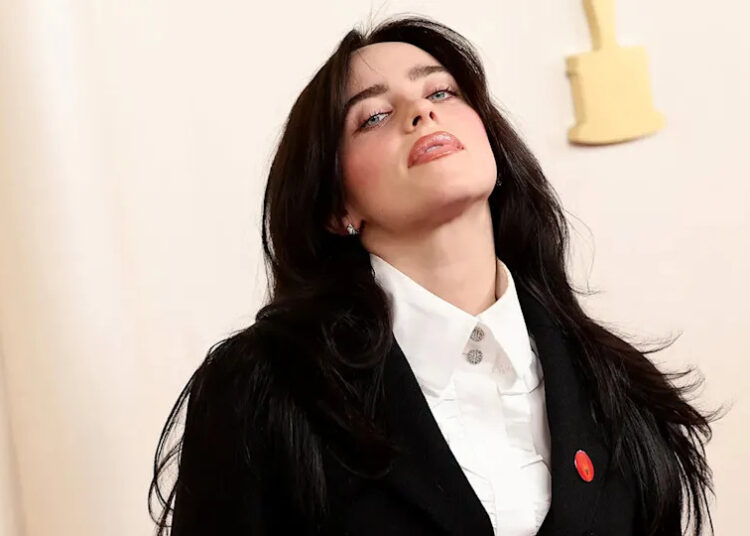 Billie Eilish tilts her head up on the carpet wearing a black suit at the Academy Awards