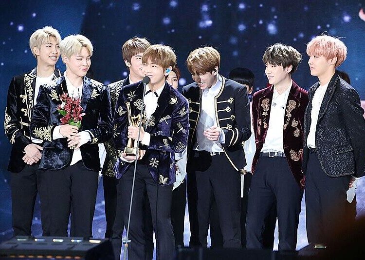 A group accepts an award on stage as one member speaks into a microphone.
