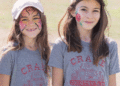 Two girls wearing white baseball caps and gray Crane t-shirts, show off their face paintings that are always a hit at the Crane Country Fair. (Courtesy photo)