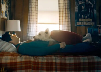 Superman, played by David Corenswet, lies on the bed recouping with Krypto the superdog resting on his chest. .