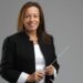 A white woman with shoulder-length brown hair wears black and white and holds a conductor's baton. Sue Samuels