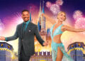 Dancing with the Stars cohosts Alfonso Ribeiro and Julianne Hough are seen in front of an image of a Disney park castle, with fireworks in the background; several fireworks on the right, behind Hough, are shaped like Mickey Mouse.