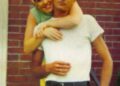 a younger dolly parton standing behind carl dean with her arms around his neck