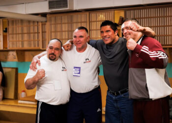 Mark Kerr (Dwayne Johnson, second from right) takes a picture with his opponent (Oleksandr Usyk, far right) after a match in "The Smashing Machine."
