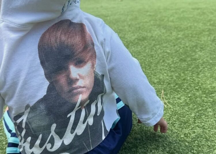 child sitting on grass wearing a hoodie with a graphic design