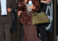 Hilaria Baldwin smiling while leaving Good Morning America studios in New York City wearing a brown outfit and carrying a Louis Vuitton handbag