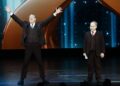 Two men in suits stand on a stage.