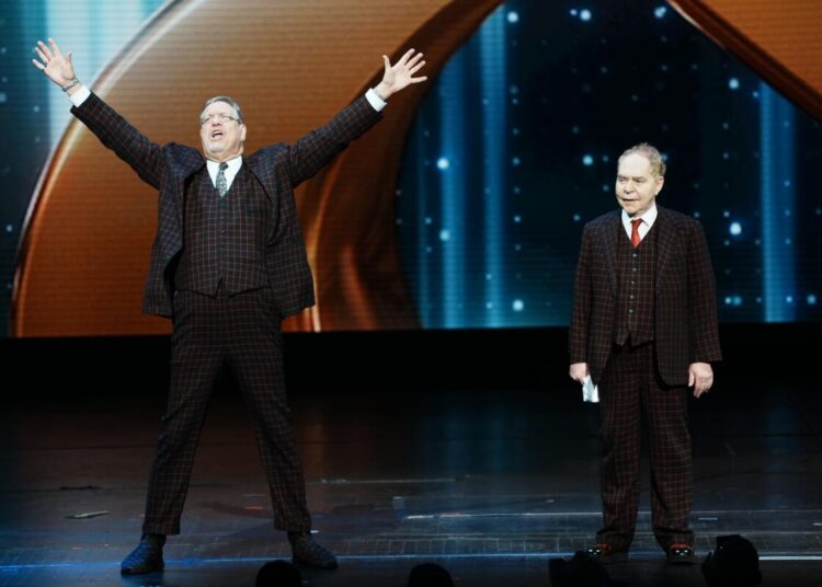 Two men in suits stand on a stage.