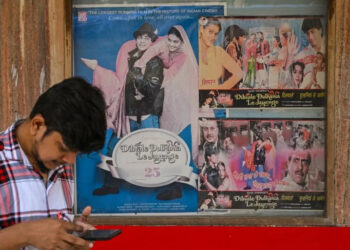 A moviegoer checks his phone whilst standing beside a poster of the popular Bollywood Hindi film 'Dilwale Dulhania Le Jayenge' in Mumbai