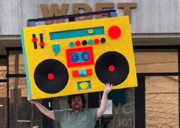 In The Groove host Ryan Patrick Hooper holds Detroit's largest boombox — designed by Detroit artist Matthew Holman — outside of WDET Studios during the 2025 spring fundraiser.