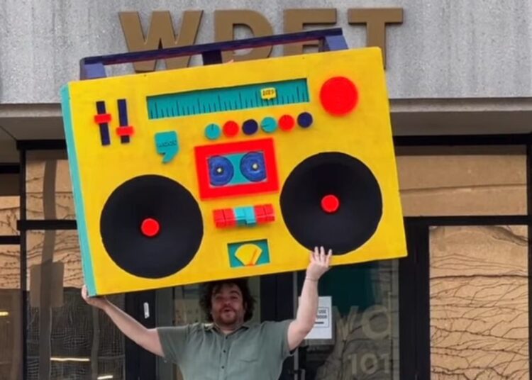 In The Groove host Ryan Patrick Hooper holds Detroit's largest boombox — designed by Detroit artist Matthew Holman — outside of WDET Studios during the 2025 spring fundraiser.