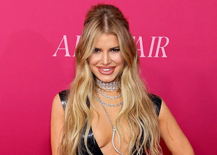 Jessica Simpson smiling on red carpet in black latex dress with plunging neckline