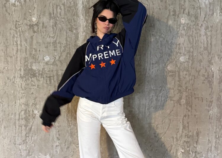 Kendall Jenner wears a track jacket, white pants, and black loafers