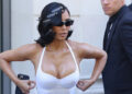 Kim Kardashian in a white dress with hair clips and sunglasses, adjusting her outfit.