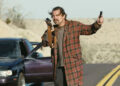 Leonardo DiCaprio as Bob holding a gun and a device in One Battle After Another.