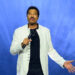 Lionel Richie performs on stage against a blue background with lights.