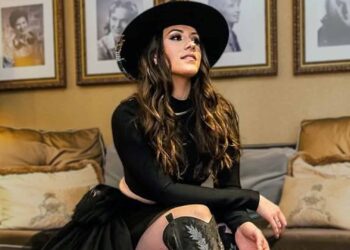 Maggie Baugh sitting confidently in a stylish black outfit, announcing her new single The Devil Win amid swirling Keith Urban rumors.