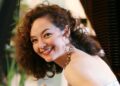 An Asian woman with brown curly hair wears formal attire in an indoor photo. Sandra Wright Shen.