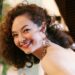 An Asian woman with brown curly hair wears formal attire in an indoor photo. Sandra Wright Shen.