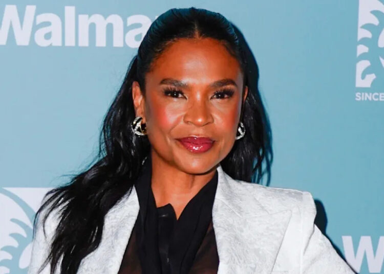 Nia Long in a white blazer poses in front of a blue background with logos.