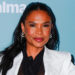 Nia Long in a white blazer poses in front of a blue background with logos.