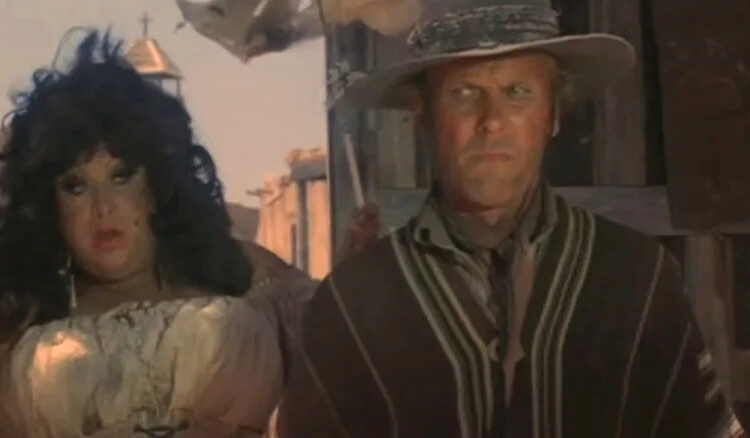 Divine as Rosie Velez and Tab Hunter as Abel Wood standing side-by-side in a western town in Lust in the Dust
