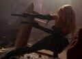 Barb firing two guns from behind a table in Barb Wire