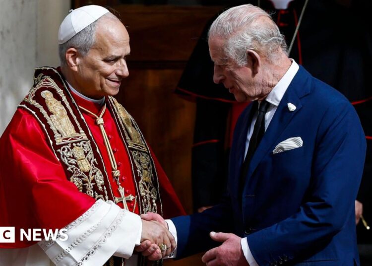 Pope Leo XIV cloaked in red shaking hands with Queen Camilla wearing all black with a black veil