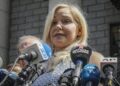 A blonde woman with a bank of microphones in front of her.