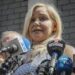 A blonde woman with a bank of microphones in front of her.