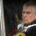 Prince Andrew in ceremonial clothes looks out a rainy window