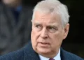 Reuters Prince Andrew has short grey hair and is gazing to one side. He is wearing a dark blue jacket, a white shirt and a red tie.