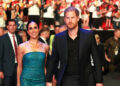Meghan Markle and Prince Harry holding hands and walking together as a crowd cheers behind them.