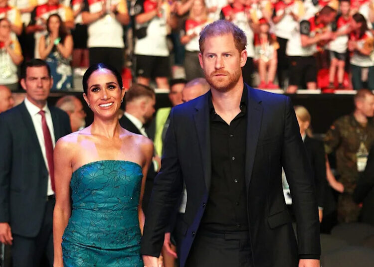 Meghan Markle and Prince Harry holding hands and walking together as a crowd cheers behind them.