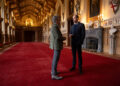 Prince William and Eugene Levy talking in a red carpeted hall at Windsor Castle