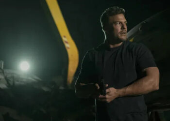 alt="Reacher holds a gun and looks to his side in Reacher season 3"